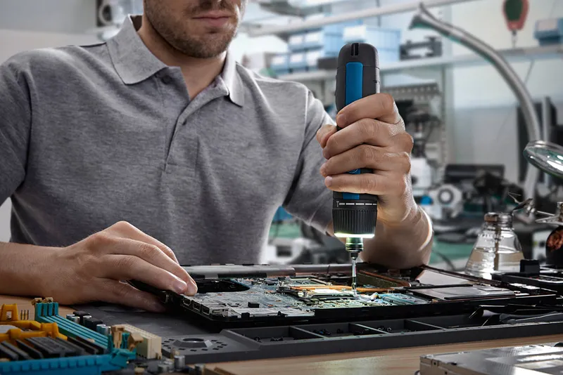 人員使用無線螺絲起子組裝電路板上的電子元件。.