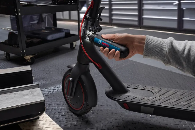 一個人用無線螺絲起子調整電動滑板車的車把。.