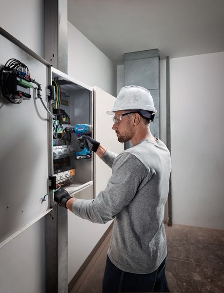 佩戴安全設備的人員使用無線電鑽在電氣面板上工作。.