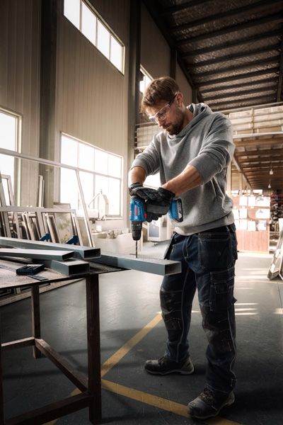 一名配戴安全設備的人員在車間內鑽入金屬梁。.