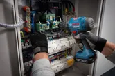 配戴安全設備的人員使用無線電鑽在電氣控制面板上操作。