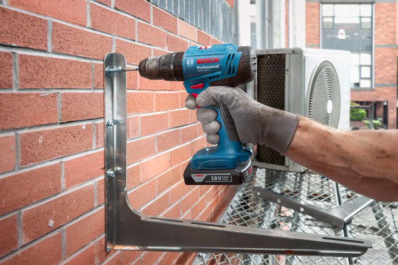 一名配戴安全設備的人員使用無線電鑽將金屬支架固定在磚牆上。.