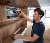 一個人使用無線螺絲起子來緊固電氣面板上的元件。.