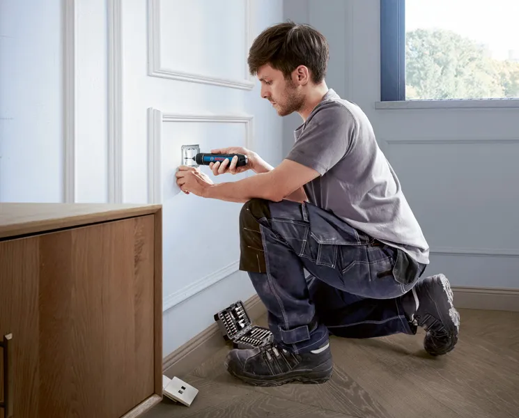 一個人使用無線螺絲起子安裝電源插座蓋。.