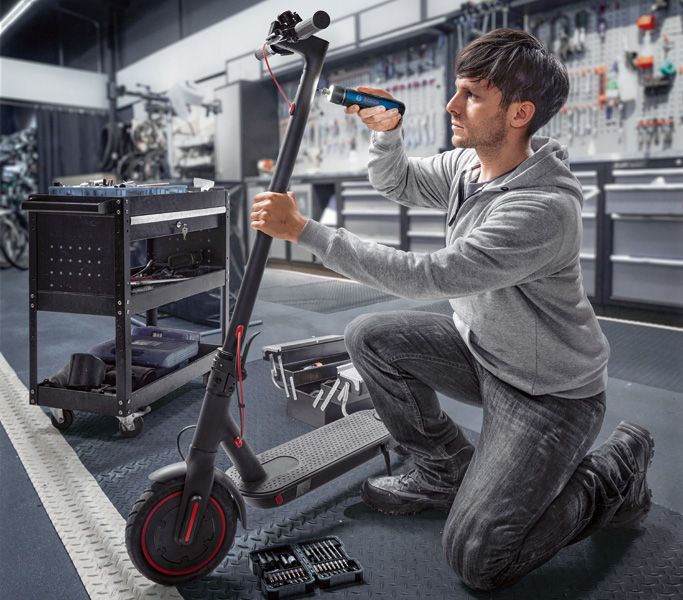 一名工人在車間使用無線螺絲起子修理電動滑板車。.