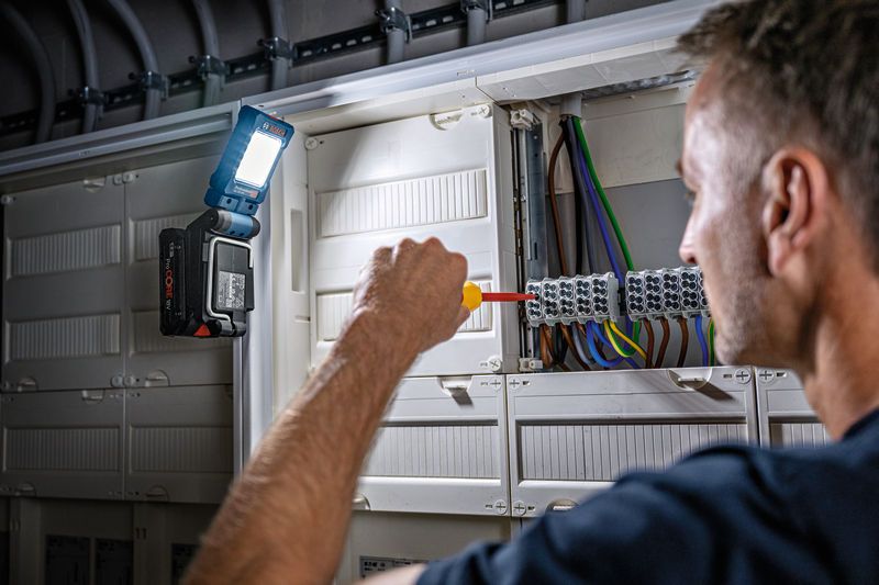 一個人使用螺絲起子在電氣面板上操作，並連接無線燈進行照明。.