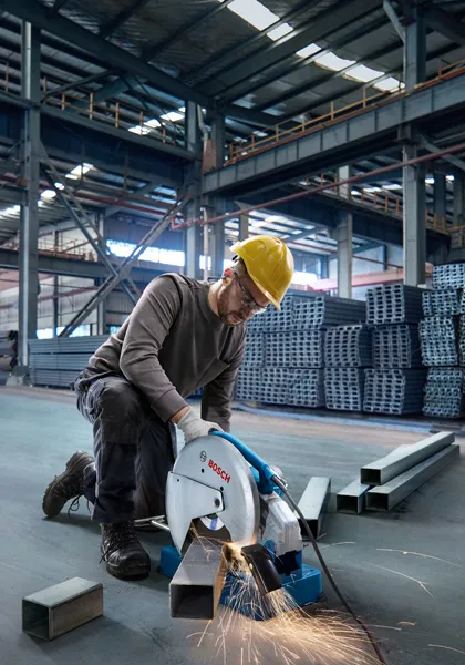 一名配戴安全設備的人員在倉庫裡用切割鋸切割金屬管。.