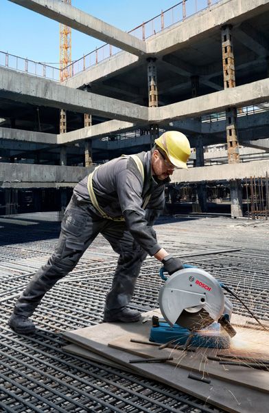 一名佩戴安全設備的人員在建築工地用切割鋸切割金屬管道。.