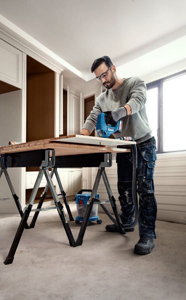 一名配戴安全設備的人員在工作台上使用曲線鋸切割木材。.