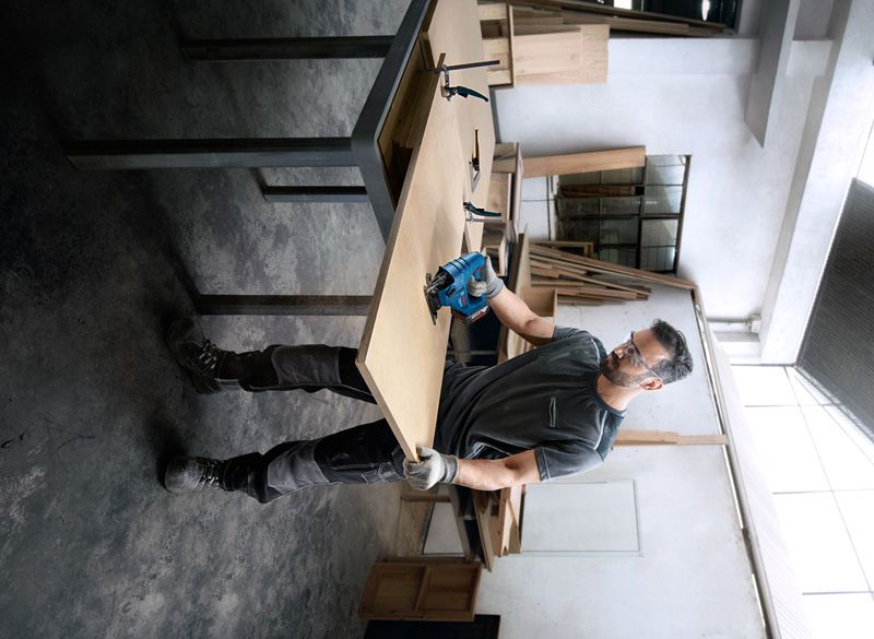 一名配戴安全設備的人員在車間使用電動工具切割木材。.