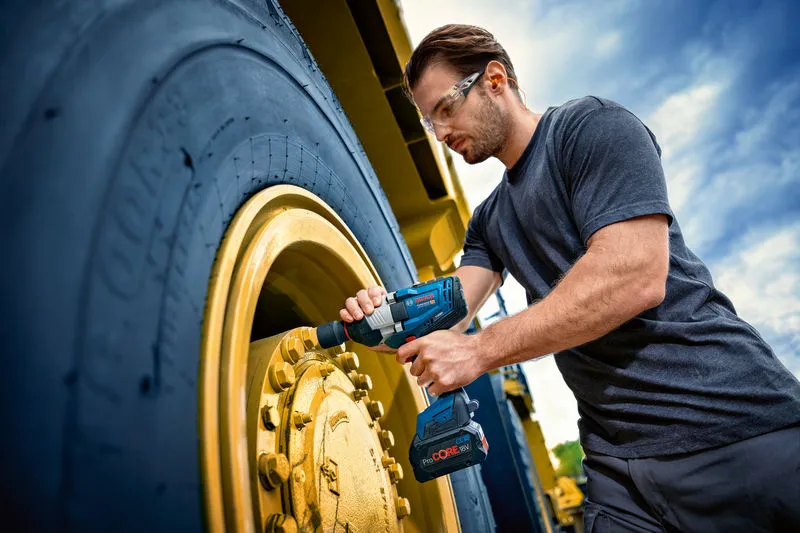 一名配戴安全設備的人使用衝擊扳手來擰緊大型車輪。.