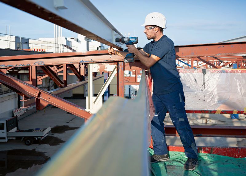 一名配戴安全設備的人員使用無線衝擊扳手來擰緊鋼樑。.