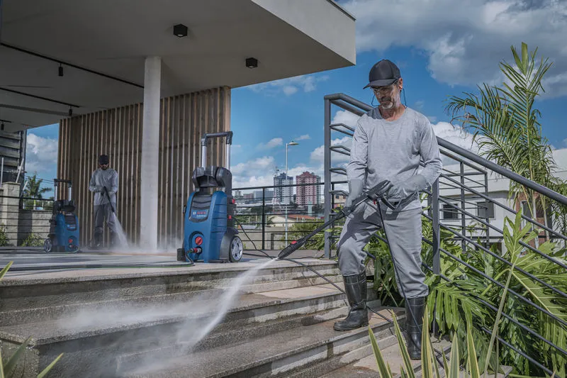 一名配戴安全設備的人員使用高壓清洗機清洗室外樓梯。.