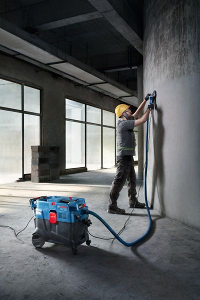 一名配戴安全設備的人員使用多用途萃取器打磨混凝土牆。.