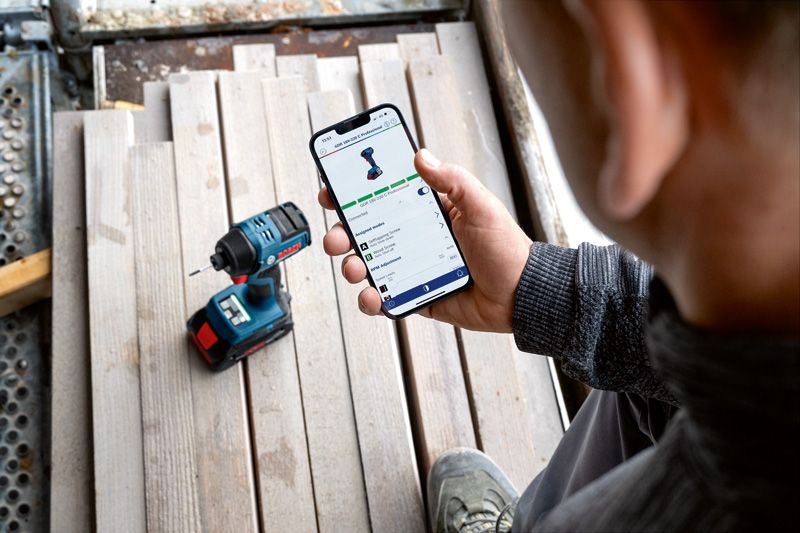 一個人在無線電鑽旁用智慧型手機檢查電動工具的應用程式功能。.