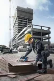 一名配戴安全設備的人員在建築工地上使用無線鋸切割膠合板。