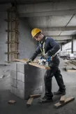 一名配戴安全設備的人員正在用圓鋸在混凝土塊上切割木材。