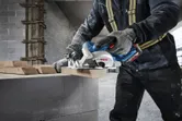 在建築工地上，一名配戴安全設備的人員正在用圓鋸切割木材。