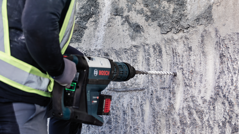 PRO SDS max-4 四溝鎚鑽鑽頭,12 x 200 x 340 mm 一名配戴安全設備的人員使用電動工具在混凝土牆上鑽孔。