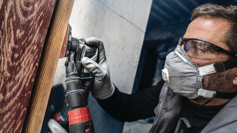 配戴安全設備的人員使用電動工具打磨木質表面。