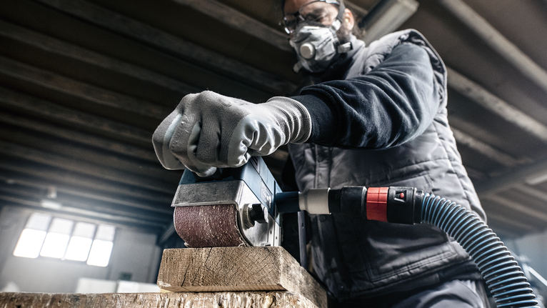 一名配戴安全設備的人員正在使用電動工具打磨木樑。