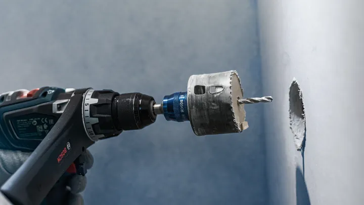 配戴安全設備的人員在牆上鑽一個圓孔。