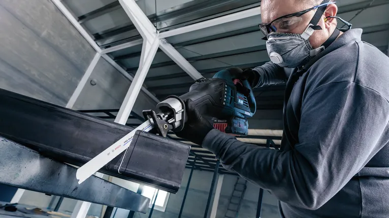 配戴安全設備的人員使用往復鋸切割鋼樑。