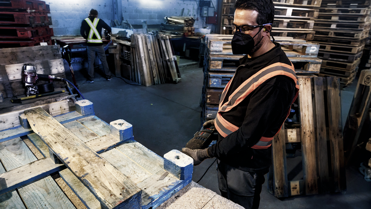 一名配戴安全設備的人員使用電動工具在木質托盤上工作。