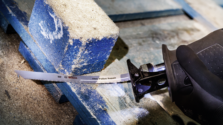 配戴安全設備的人員使用往復鋸切割木托盤。