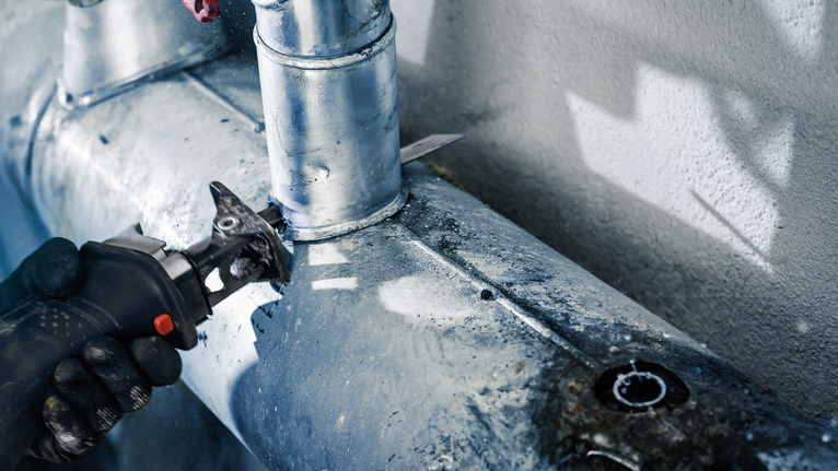 配戴安全設備的人員使用電動工具切割金屬管路。