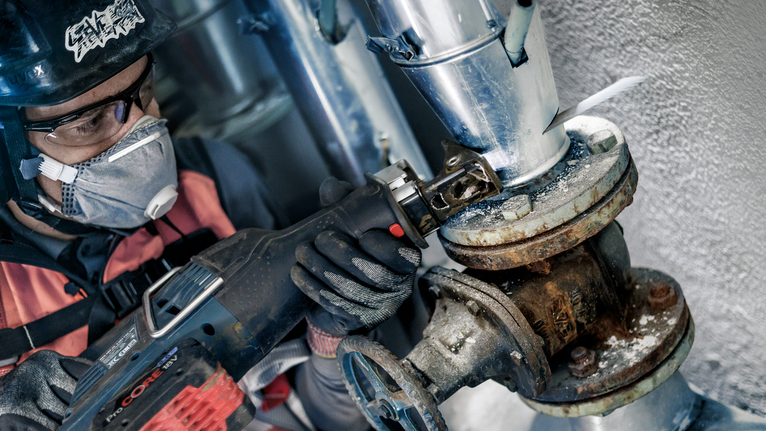 一名配戴安全設備的人員使用往復鋸切割腐蝕的管道。