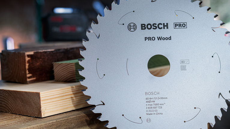 PRO Wood 充電式圓鋸片,216 x 1.7 x 30 mm,T48 帶有鋒利鋸齒的圓鋸片位於堆疊的木樑旁。