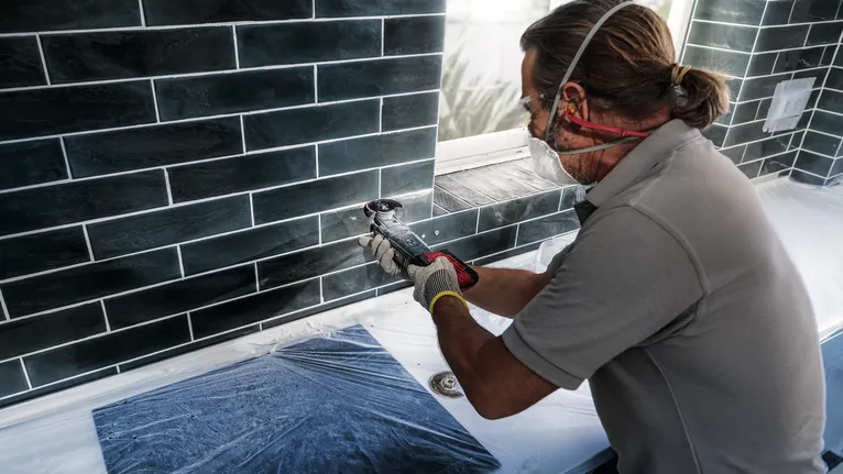 配戴安全設備的人員使用電動工具切割窗戶下方的磁磚。