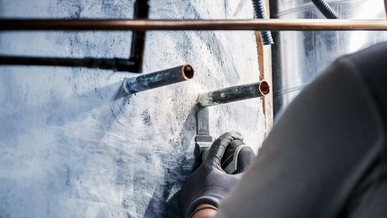 配戴安全設備的人員使用電動工具切割金屬管路周圍的牆壁。