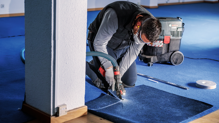 一名配戴安全設備的人員在室內使用電動工具切割藍色地毯。
