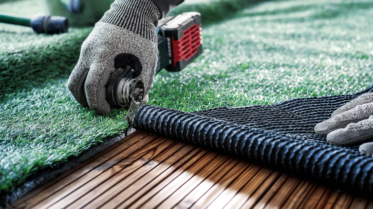 穿著安全設備的人員正在修剪木質甲板上的人造草坪。