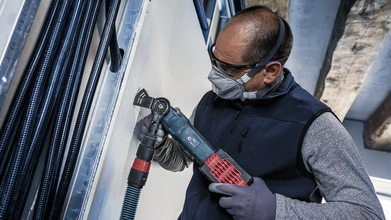 一名配戴安全設備的人員正在使用電動工具切割乾牆。