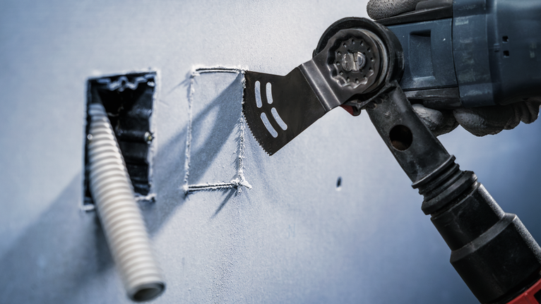 配戴安全設備的人員使用多功能工具在乾牆上切出一個整齊的開口。