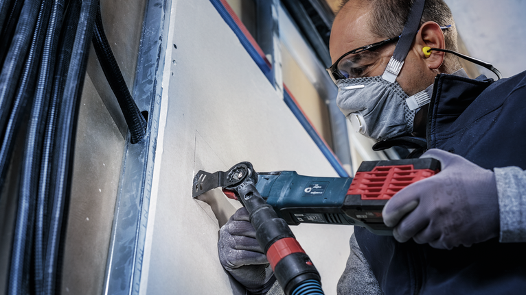 配戴安全設備的人員使用電動多功能工具切割乾牆。