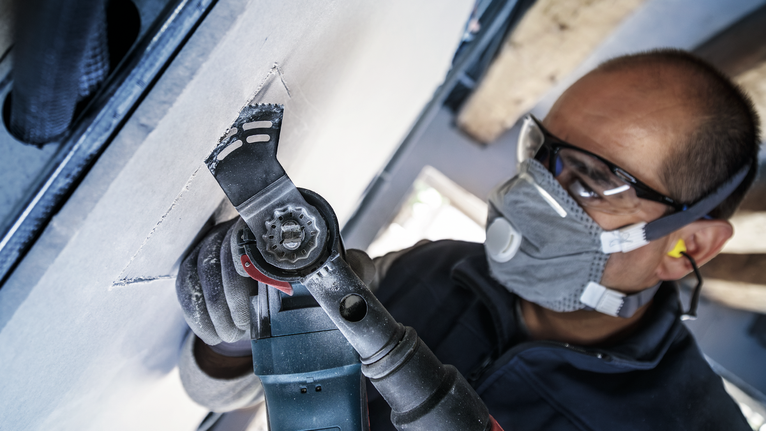 一名配戴安全設備的人員正在使用電動工具切割乾牆。