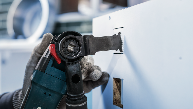 配戴安全設備的人員使用電動工具在乾牆上切出一個矩形孔。