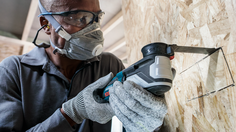 配戴安全設備的人員使用電動工具在木頭上切出一個方形開口。