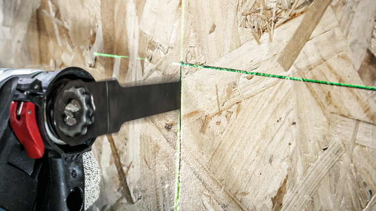 一名配戴安全設備的人員使用往復鋸沿著綠色指導線切割木材。