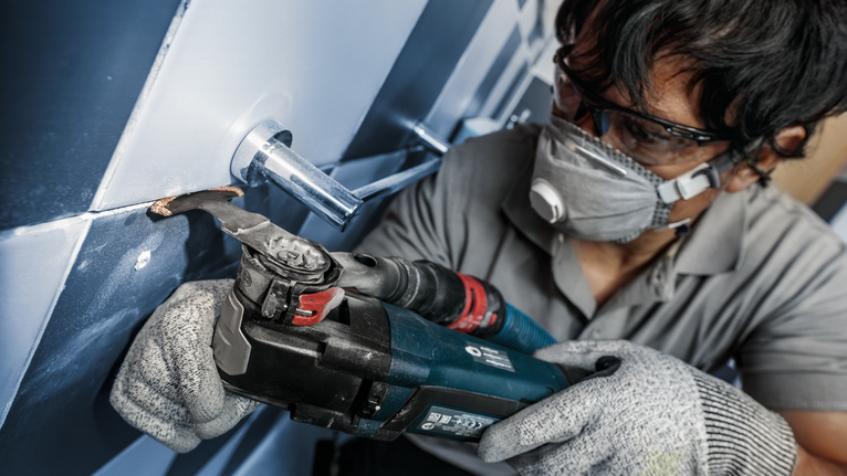 一名佩戴安全設備的人員使用電動工具切割管道周圍的瓷磚。