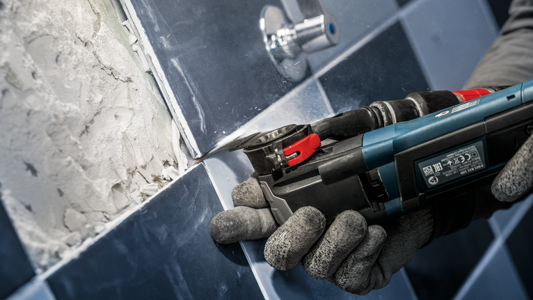 配戴安全設備的人員使用電動多功能工具從磁磚上移除水泥漿。