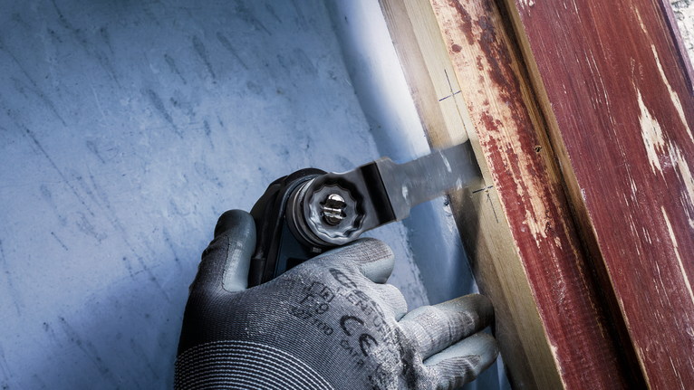 配戴安全設備的人員使用多功能工具切割油漆表面附近的木材。