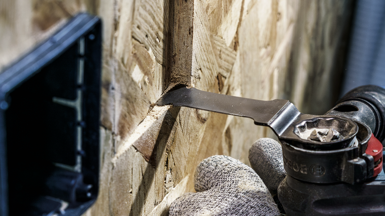 配戴安全設備的人員使用多功能工具在木鑲板上切割出一個窄槽。