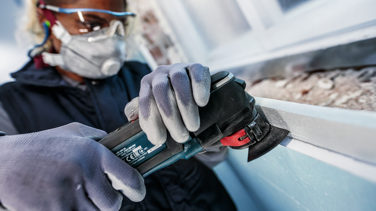 一名配戴安全設備的人員正在使用電動工具打磨窗框。