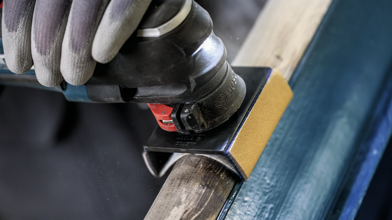 配戴安全設備的人使用電動多功能工具打磨木材。
