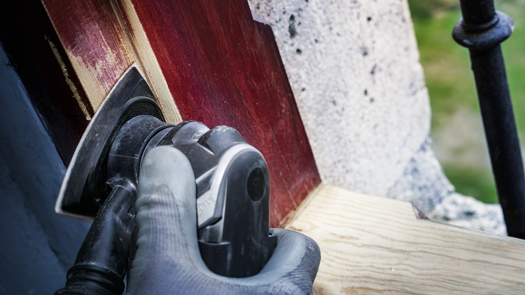 一名配戴安全設備的人員正在使用電動工具打磨塗漆的木材。